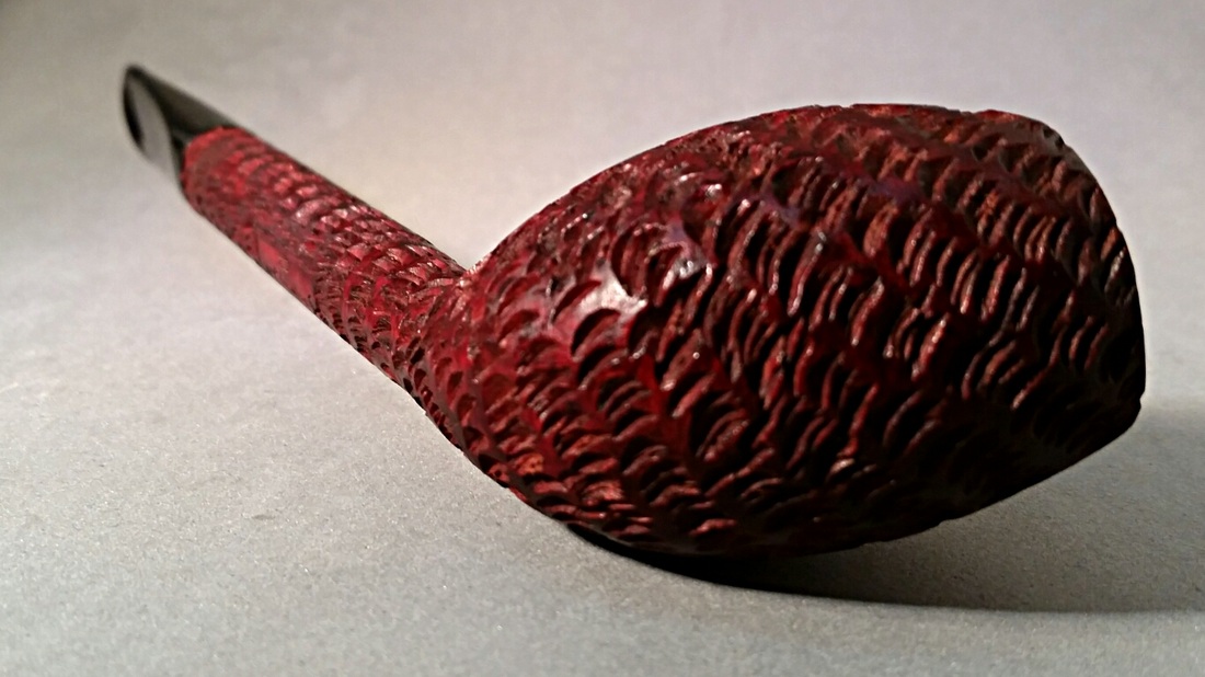 Deep red textured tobacco pipe with carved scale-like pattern against a dark background, warm and contemplative mood